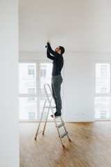 home owner standing on ladder fixing light installation