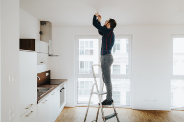 home owner standing on ladder fixing light installation