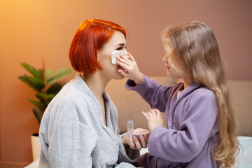 Daughter makes mom make up at home on bed.