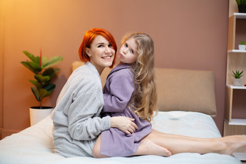 Happy mother and her baby daughter girl on bed in bedroom.