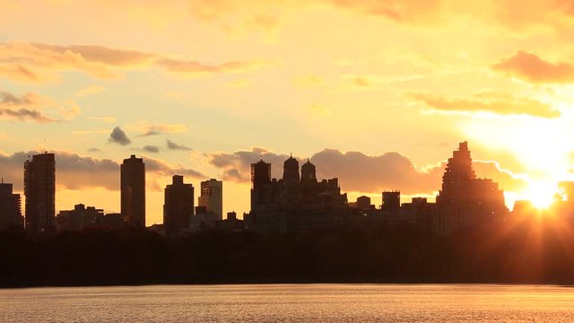 Sky, Clouds and Central Park Reservoir glow and illuminate by sunset. Central Park West Residences become silhouettes. Image was captured from Central park.