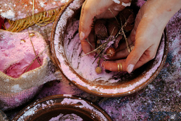 A girl in a national costume is preparing a potion in pottery sitting on a traditional carpet....