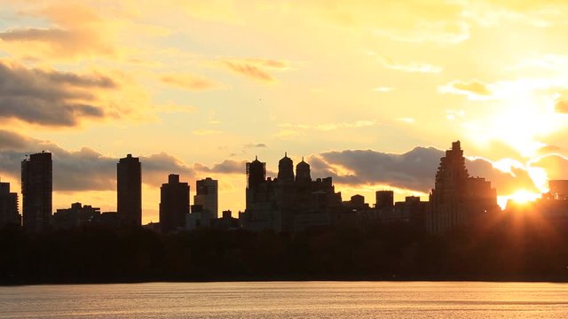Sky, Clouds and Central Park Reservoir glow and illuminate by sunset. Central Park West Residences become silhouettes. Image was captured from Central park.