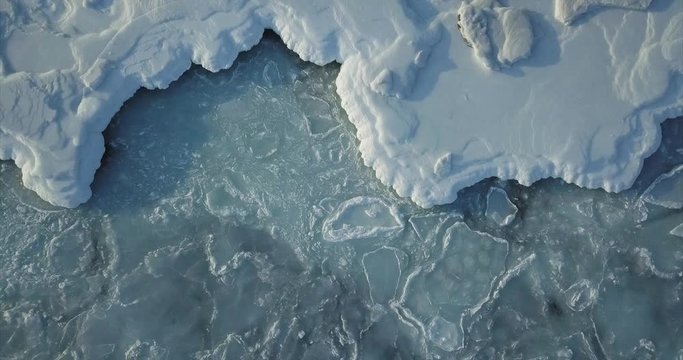 Aerial top view of sea surface with ice on it. Ice floes are moving with sea waves. Winter concept