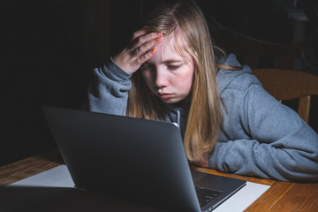 Stressed teen girl working/studying with a laptop at night on a desk.