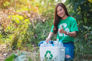 A beautiful asian woman making thumbs up hand sign while collecting garbage plastic bottles into a...