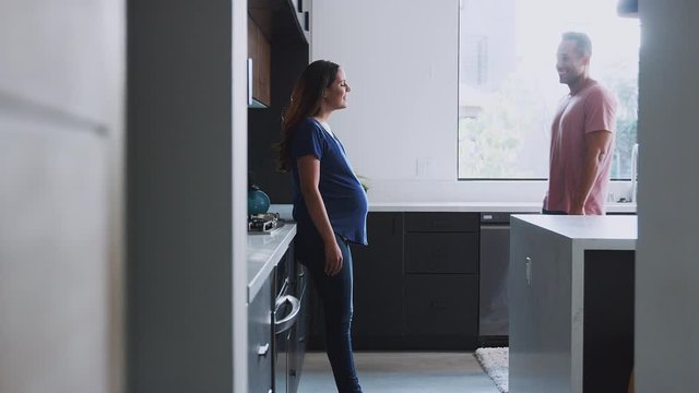 Loving Hispanic Husband With Pregnant Wife At Home In Kitchen Together