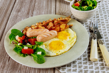Meal for breakfast egg, sausage, bacon, salad with fork and knife.