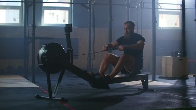 Slow motion: Rower trains, cardio athlete training. One man in an atmospheric fitness room in the sunlight in a rowing machine.