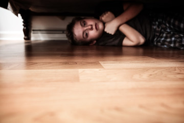 Fototapeta na wymiar Scared boy hiding under the bed