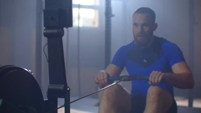 Slow motion: One men rower trains in a fitness room on a rowing machine