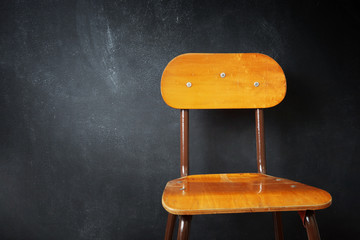 Empty wooden school chair against a black chalkboard in school