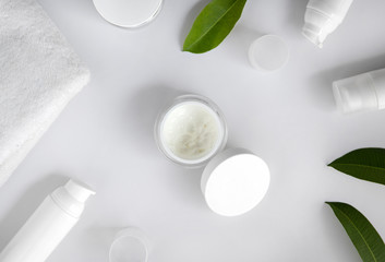 Cosmetic cream, towel and leaves on white background