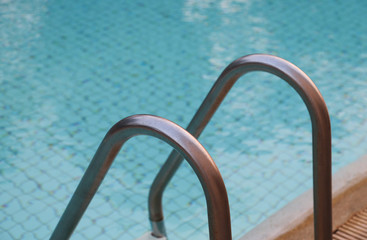 Obraz na płótnie Canvas Closeup of stainless handrail of ladder at swimming pool with water surface background.