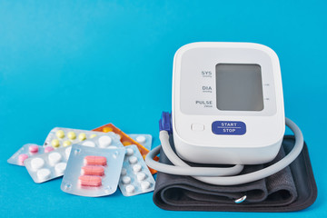 Digital blood pressure monitor and medical pills on a blue background. Healthcare and medicine concept