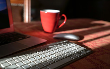 Laptop with wireless keyboard and mouse and coffee in red cup. Work from home.