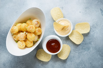Bowl of fried potato balls with parmesan, potato chips and dipping sauces. Flatlay on a light-blue stone background, studio shot