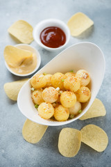 White bowl with roasted potato balls, potato chips and dips over light-blue stone surface, vertical shot, selective focus