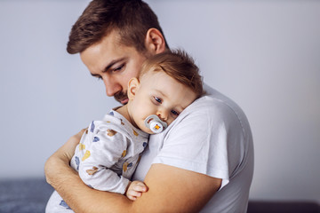 Sleepy adorable little boy with beautiful blue eyes having pacifier in his mouth and leaning on...
