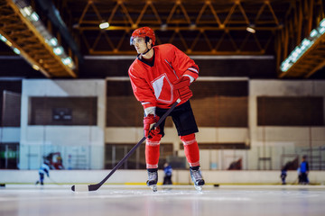 Full length of handsome hockey player skating, holding stick in his hands and trying to play...