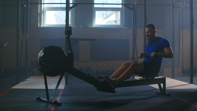 Slow motion: one man in an atmospheric fitness room in the sun in a rowing machine