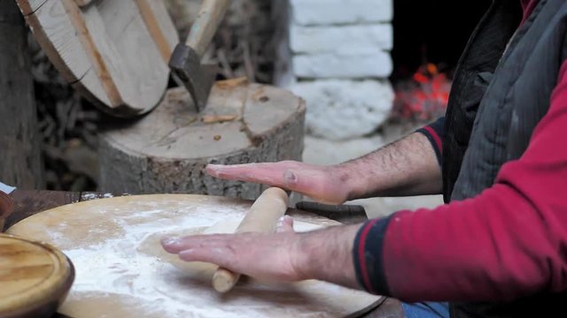 Man rolls dough with a rolling pin for baking flatbread in the medieval oven. 