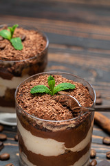 Classic tiramisu dessert in a glass cup and pieces of chocolate on wooden background
