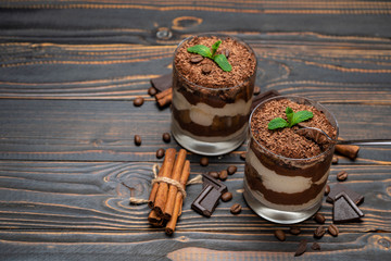Classic tiramisu dessert in a glass cup and pieces of chocolate on wooden background
