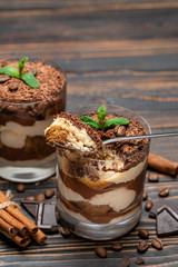 Classic tiramisu dessert in a glass cup and pieces of chocolate on wooden background