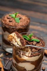 Classic tiramisu dessert in a glass cup and pieces of chocolate on wooden background