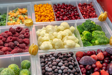 Frozen vegetables, fruits and berries are in plastic boxes. In the center of the frame is cauliflower.