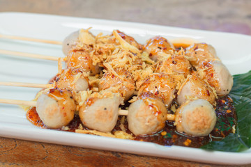 Grilled meat balls on sticks with spicy sauce on top with deep fried shallots.