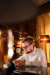 people and technology concept - happy man with smartphone drinking beer and reading message at bar or pub