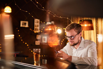 people and technology concept - happy man with smartphone drinking beer and reading message at bar or pub