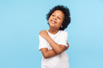 I love myself. Portrait of adorable optimistic little boy with curls embracing himself and smiling,...