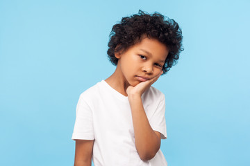 Portrait of lazy bored preschool boy with curly hair leaning on hand and looking depressed, child...