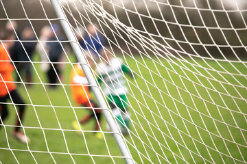 boys playing football match from behind goal net with intentional blur of identities