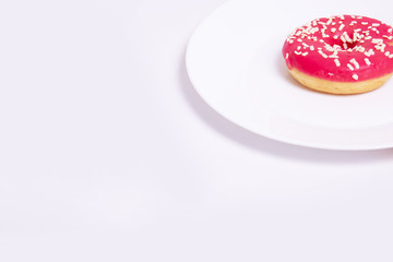 doughnut with pink icing lies on a white plate on a white background with copy space