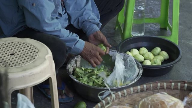 Handheld slow motion shot of a man in a long sleeves peeling a mango to sell, Philippines
