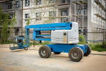 Blue working platform on background of building. Mobile crane at construction site. Boom lift outdoors. Telescopic elevator for rent