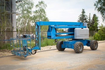 Blue working platform on background of building. Mobile crane at construction site. Boom lift outdoors. Telescopic elevator for rent