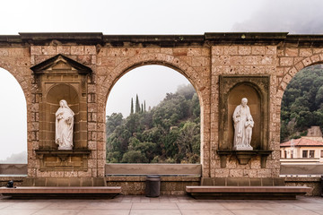 Fototapeta premium Arch of Montserrat Monastery in foggy winter day. Hiking religious destination.