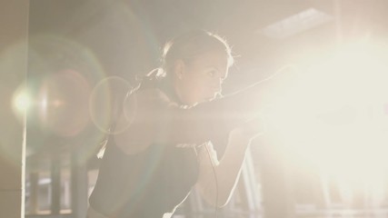 Athletic female doing shadow boxing workout in urban area. Shot in slow motion with dusty particles shimmering in the sunlight.