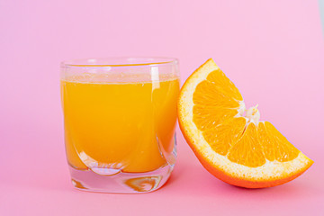 Orange juice and piece of orange with pink background.