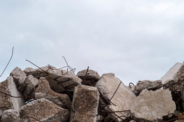 A pile of large gray concrete fragments with protruding fittings against a cloudy sky.
