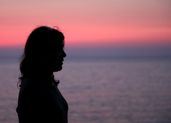 black profile of young woman with long hair at the sea with pink