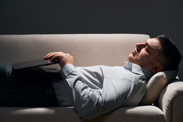 Obraz premium businessman is lying on the sofa with laptop and resting