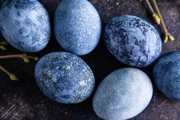 Happy easter concept. Multicolored easter painted eggs in blue tones and branches with buds on a brown background.