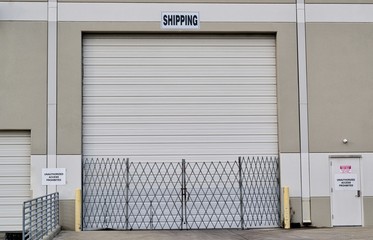 Single closed loading dock door with security gate and shipping sign above it. Warehouse...