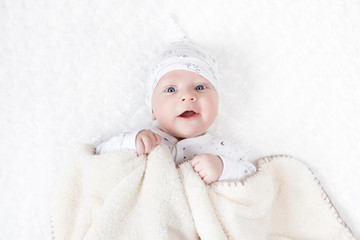 four-month-old white boy with blue eyes lies on a white blanket and take cover with him